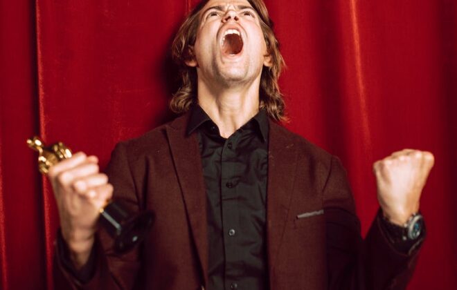 a man in a suit celebrating while holding an oscar